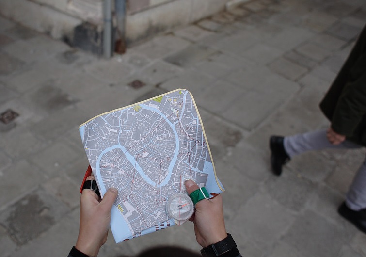 mani che reggono una mappa da orienteering e una bussola in una calle veneziana