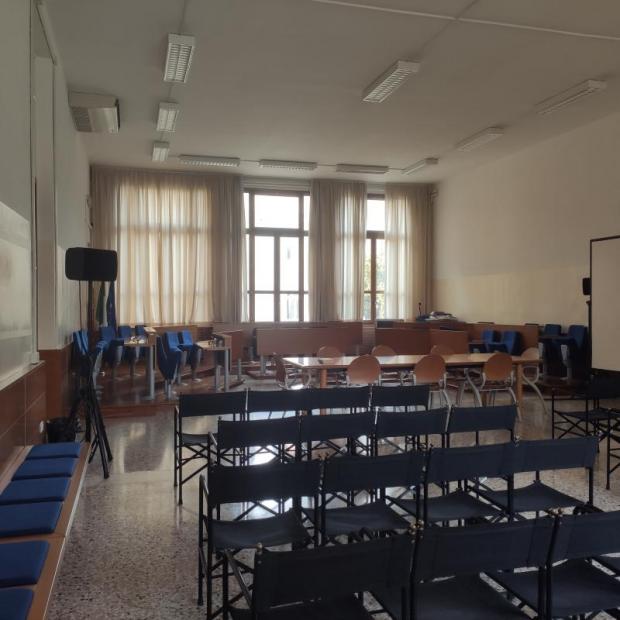 Sala consiliare con sedie per pubblico in primo piano e tavolo consiglieri in fondo
