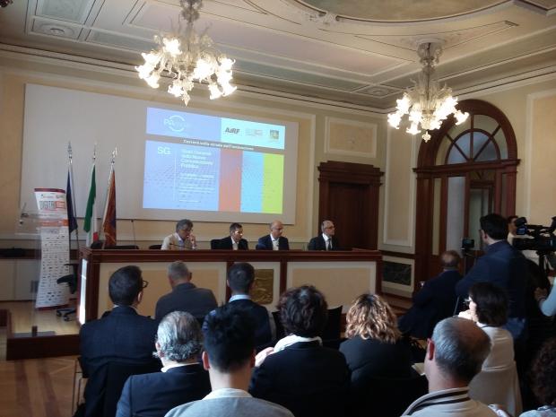 Foto del convegno in corso, con pubblico di spalle e relatori