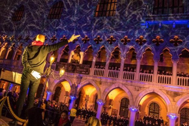 direttore, di spalle, dirige il proprio coro posizionato nella Loggia di Palazzo Ducale a Venezia