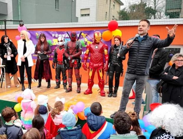 Gruppo di persone su un palco, tra cui cinque cosplayer vestiti da supereroi. Sono guardati da un pubblico di bambini di spalle