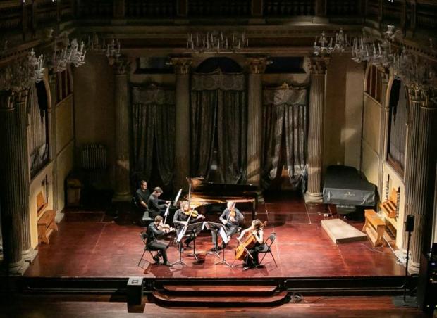 Cinque musicisti sul palco, uno al pianoforte, quattro con violini, viole e violoncello