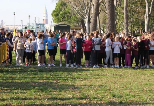 Bambine sulla linea di partenza di una gara di corsa campestre in un parco. Sullo sfondo un campanile