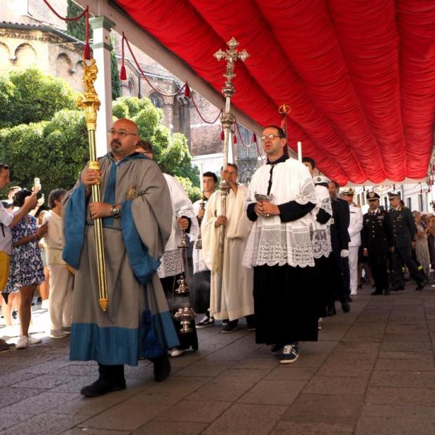 Processione cristiana sotto un tendone. Ai lati, il pubblico, tra cui persone che scattano foto con lo smartphone