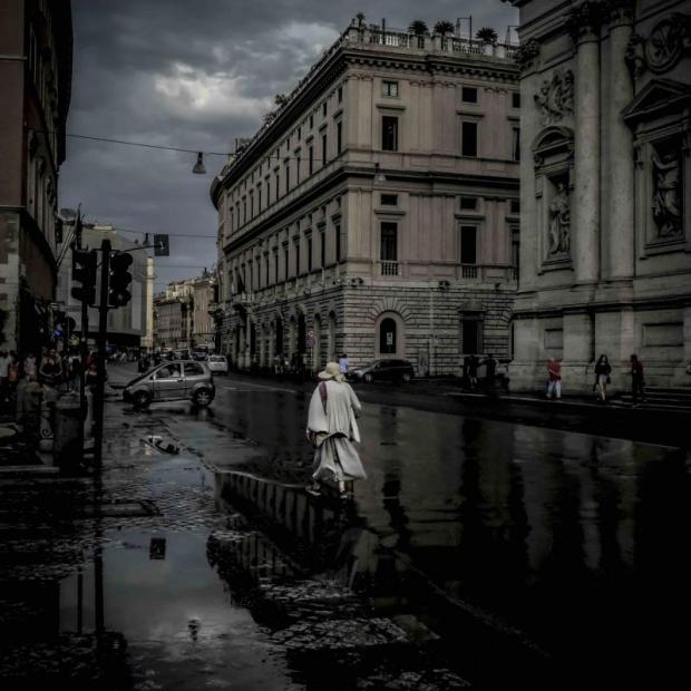 Donna vestita di bianco e col cappello passeggia per le vie allagate di una città dopo un temporale