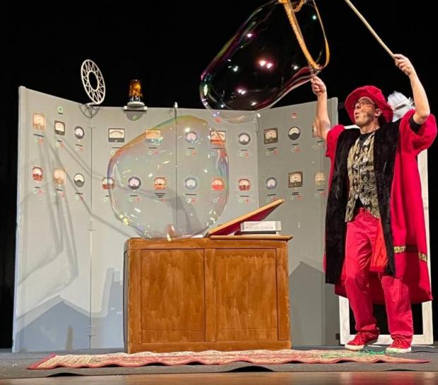 Un uomo in costume rinascimentale fa delle bolle di sapone giganti su un palco