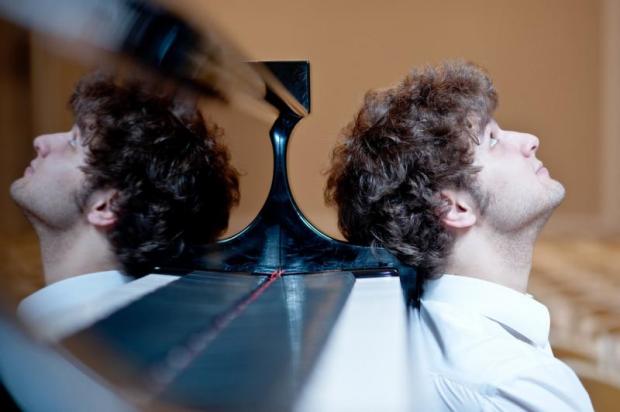 Pianista appoggiato alla testiera del suo strumento; la sua testa si riflette sulla superficie lucida della cassa armonica