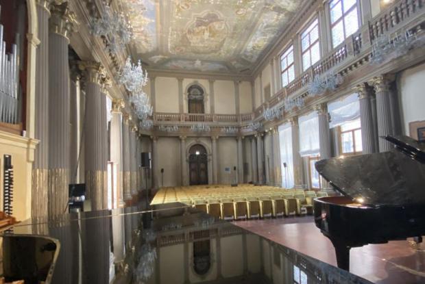 Sala da concerti decorata con stucchi, tendaggi e lampadari. A destra, in primo piano, un pianoforte