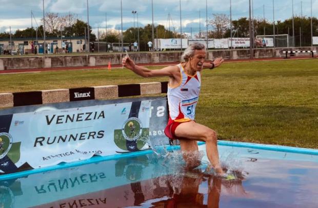 Podista in gara nei 3000 siepi che ha appena saltato un ostacolo atterrando in una fossa del percorso