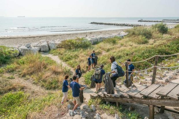 volontari scendono in spiaggia con dei sacchi per ripulirla dai rifiuti