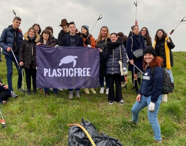 Una quindicina di persone posa su un prato reggendo uno striscione con la scritta "Plastic free" e il disegno di una tartaruga