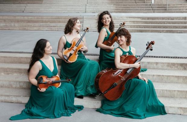 Quattro giovani musiciste con in mano i loro strumenti a corda, vestite di verde e sedute su degli scalini