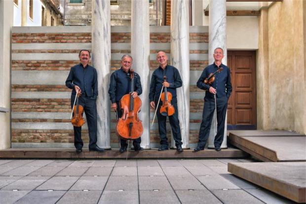 Componenti di un quartetto d'archi in posa in piedi con i loro strumenti davanti quattro colonne