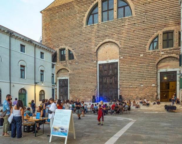 Modifica della foto fornita di Enrico Fiorese, per gentile concessione di TBA21. “Tavole Conviviali in Campo”, Ocean Space. Folto gruppo di persone di fronte a una chiesa, in un campo veneziano