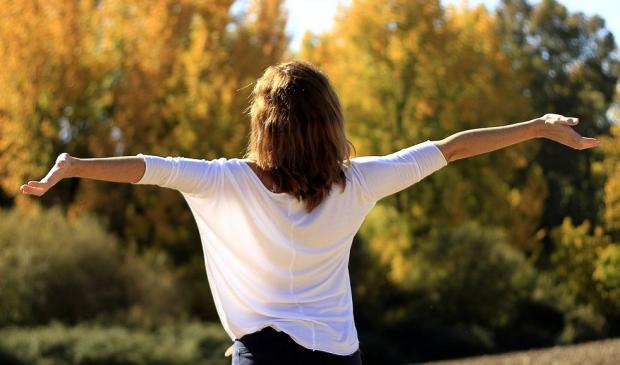 donna girata che allarga le braccia nel verde