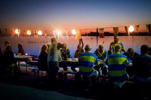 Tavolata per cena all'aperto allestita su una riva di fronte alla laguna di Venezia