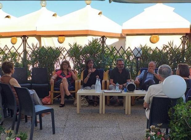 Conferenza all'aperto: relatori visti di fronte, pubblico di spalle