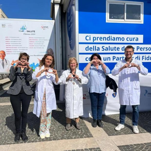 Cinque persone in riga, tra cui tre medici in camice, fanno il segno del cuore con le mani
