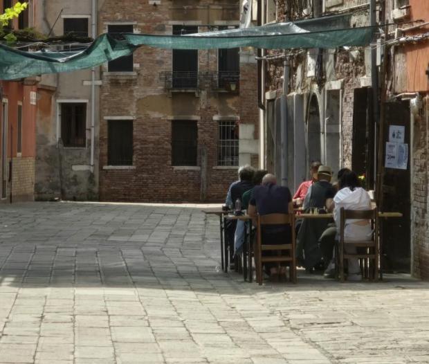 Tre coppie di persone giocano a scacchi seduti all'aperto in una strada veneziana